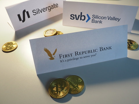 Munich, Germany Bavaria - February 25, 2023: Silicon Valley Bank, First Republic Bank, and Silvergate Capital paper logos with Bitcoin and Dogecoin cryptocurrency.