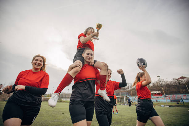 Group of women, happy female rugby team players on celebrating on a rugby field outdoors together, they won a trophy.