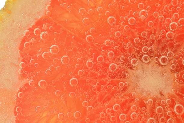 Slice of grapefruit in sparkling water. Grapefruit slice covered by bubbles in carbonated water. Grapefruit slice in water with bubbles stock photo