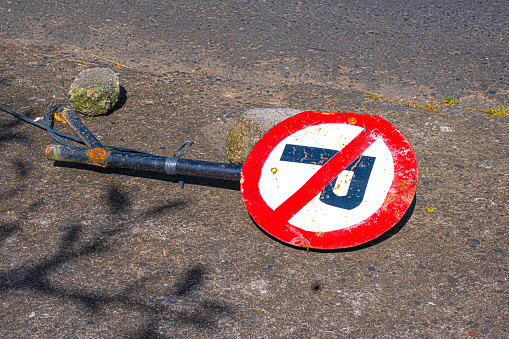 Red and white round no parking sign with black rusted pole laying on pavement