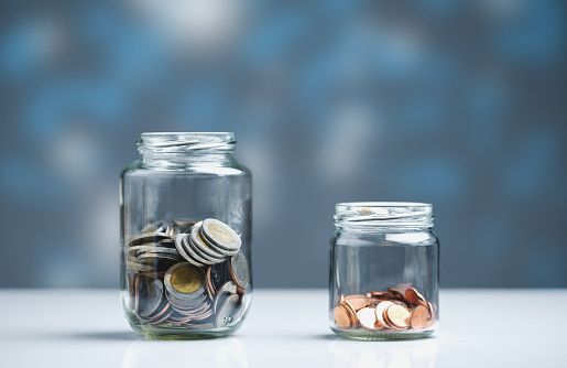 Coins saved in two separate glass jars. Income sharing concept for spending and savings.