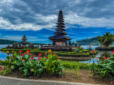 An early morning view of a Hindu Temple in the middle of the lake at the mountain of Bedugul Region in Bali. With clear blue sky and calm water decorated with colourful plants and everything feel peace and calm.