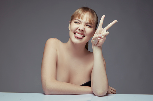Portrait of beautiful young woman sticking out her tongue while making peace sign with her hand.