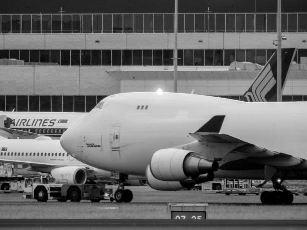 A DHL - Atlas Air Boeing B747-46N, registration N453PA, being towed from the maintenance area near to the domestic terminal, across the main runway, past the international terminal (in the background) to the parking area near the fire station at Sydney Kingsford-Smith Airport.  It arrived at 7am on 9 March 2023 and departed at 9pm on 13 March 2023. The navigational warning light is illuminated on the roof.  In the background is the fuselage of a Qantas 737-838, registration VH-XZD, at the departure gate before flying to Denpasar as flight QF43.  Also in the background is a Singapore Airlines A350-941, registration 9V-SHP, soon departing to Singapore as flight SQ242.  This image was taken from near Shep's Mound, a public viewing area off Ross Smith Avenue, on an overcast evening on 12 March 2023.