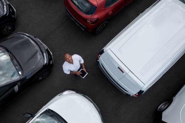 verkäufer mit einem tablet, während er von autos im autohaus umgeben ist - car old african descent car salesperson stock-fotos und bilder