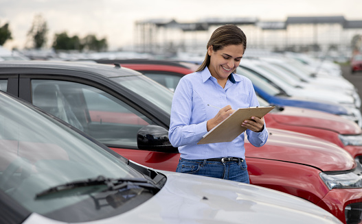 Portrait of a happy Latin American saleswoman working outdoors at a car dealership and smiling