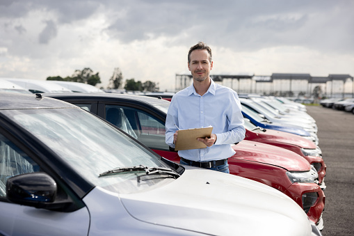 Portrait of a Latin American salesman working outdoors at a car dealership - automobile industry concepts