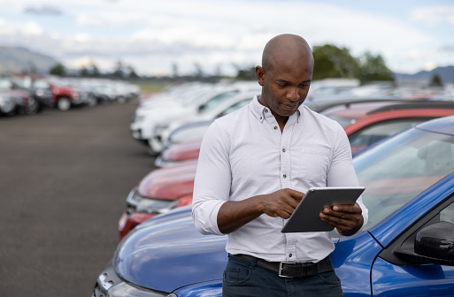 African American car salesperson working at a car dealership using a tablet - automobile industry concepts