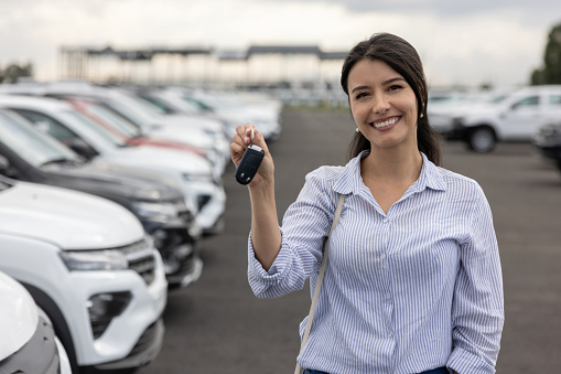 Portrait of a happy Latin American woman at the dealership holding the keys of her new car - car ownership concepts
