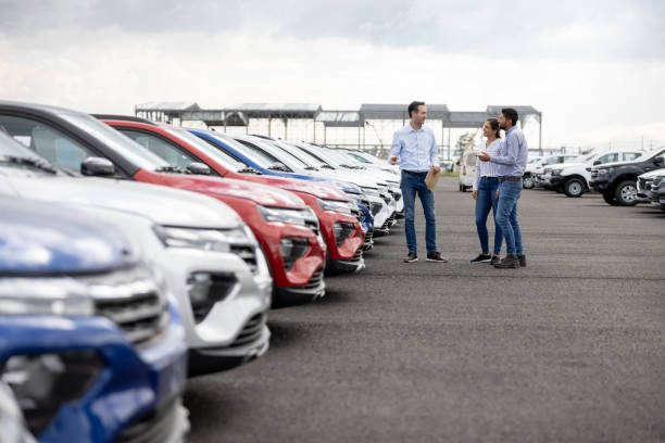 Salesman showing cars to a couple at the dealership Happy salesman showing cars to a couple at the dealership - car ownership concepts showroom stock pictures, royalty-free photos & images