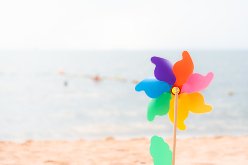 Rainbow pinwheel at beach against sea and blue sky.