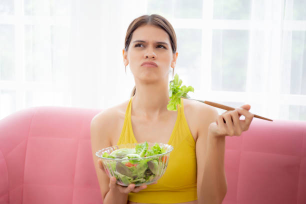 istock Young caucasian woman sitting on sofa eating vegetable salad while feeling dislike and expression disgusted, woman emotion frustrated with anorexia vegetarian and hate, nutrition food concept. 1473405031