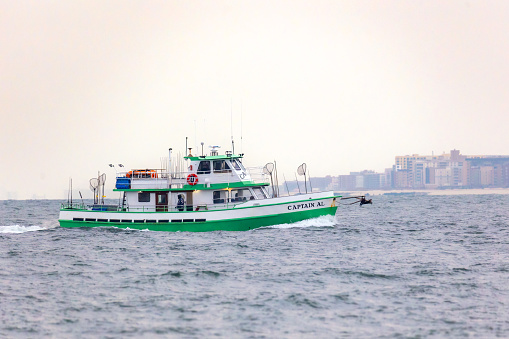 Point Lookout, New York - January 10, 2023 : The Captain Al, a charter wreck fishing boat, sailing back to shore with Long Beach Long Island in the background