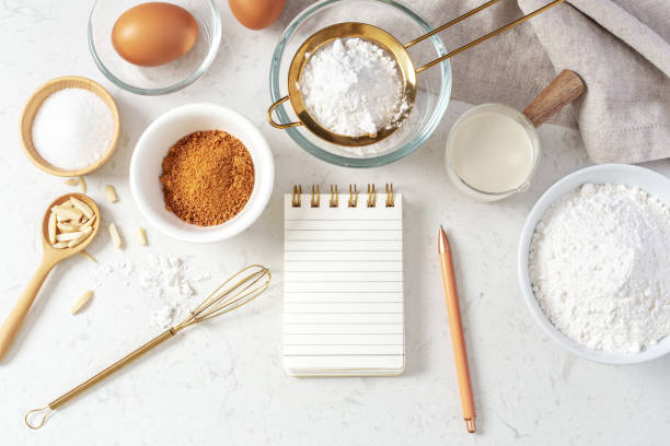 istock Baking pastry or cake ingredients with notebook and pen, sifting flour, brown sugar, eggs and milk with utensil on marble table 1473415941