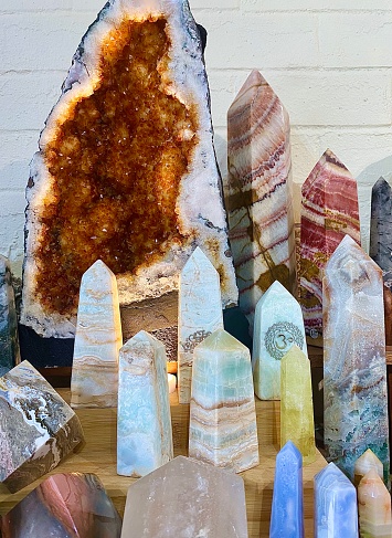 Vertical close up of a group of large crystal point & geode cave clusters varieties sparkling together on display against white wall