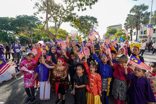 George Town, Penang, Malaysia - Aug 31 2022: Group of children wear traditional costume raise the Malaysia flag during celebration Independence day