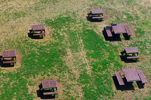 Aerial view of empty wooden park bench and wooden tables in sunny day.