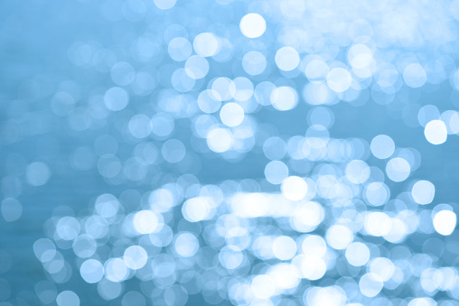 Defocused blue sea water surface with shiny bokeh lights.