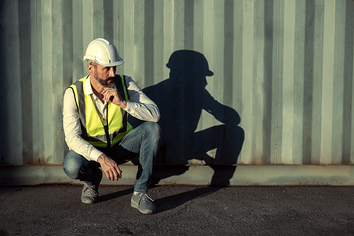 Engineer or worker sit close to cargo container look like tired and serious after work in workplace area.