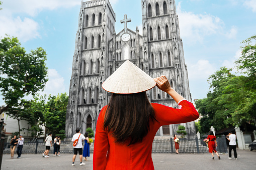 Young Asian woman tourist in Ao Dai (traditional Vietnamese dress) sightseeing at St Joseph's Cathedral church in Hanoi, Vietnam. Close up, copy space