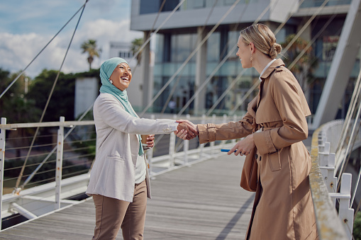 Business woman, handshake and partnership in the city for agreement, trust or deal on a bridge. Happy muslim woman employee shaking hands with colleague in meeting, greeting or introduction in Dubai