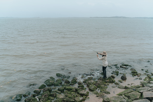 Asian chines woman standing on rocks fishing into the waters of the vast ocean
