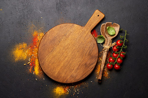 Empty cutting board over various spices on stone table. Frame with copy space for your menu or recipe
