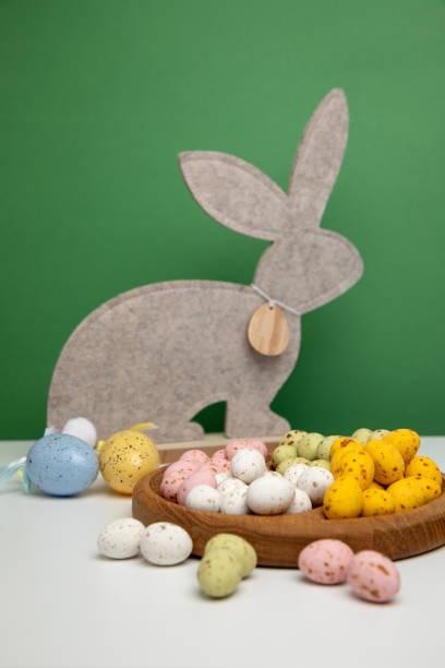 istock Multi-colored chocolate decorative eggs in wooden plate and gray rabbit on a green background. Happy Easter background 1473434918