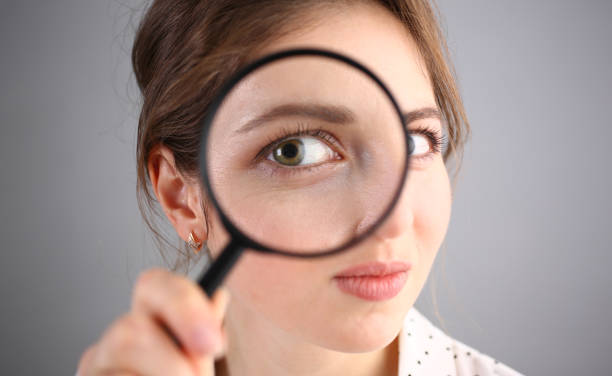 istock Inquisitive young woman looking through magnifying glass 1473435255