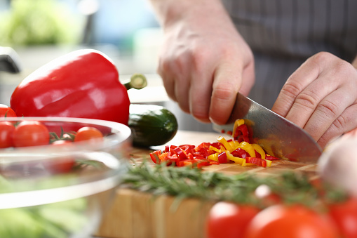 Hands of cook cut yellow and red peppers on cutting board with other vegetables on table in kitchen. Cooking fresh vitamin tasty salad concept