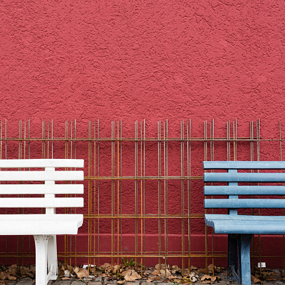 Partial view of two benches in front of steel mats and a red wall