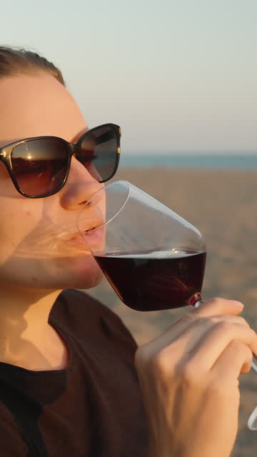 A romantic date on the seashore, a young woman holding a plate of meat and salad and drinking wine. Vertical video Social Media