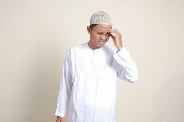 portrait of attractive asian muslim man in white shirt having a migraine, touching his temple. headache disease concept. isolated image on gray background - pusing imagens e fotografias de stock