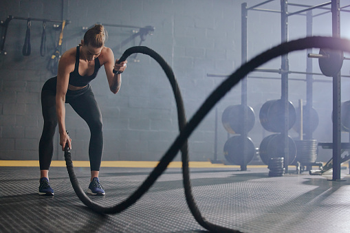Exercise, battle ropes and cardio with a woman in gym for a workout to increase strength or endurance. Fitness, training and power with a serious female athlete bodybuilding for power or health