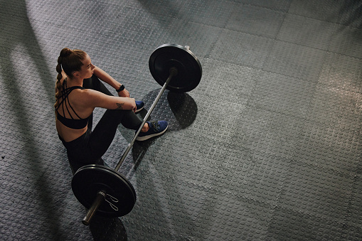 Fitness, mockup and weightlifting with a bodybuilder woman taking a break in a gym after exercise from above. Workout, training and rest with a strong female bodybuilding athlete sitting on a floor