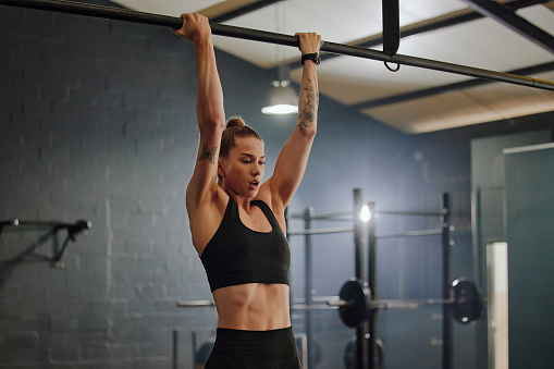 Fitness, strong and woman in the gym for pull ups, strength training and cardio. Health, serious and girl doing a workout, exercise or practice for bodybuilding, physical activity or muscle on a bar