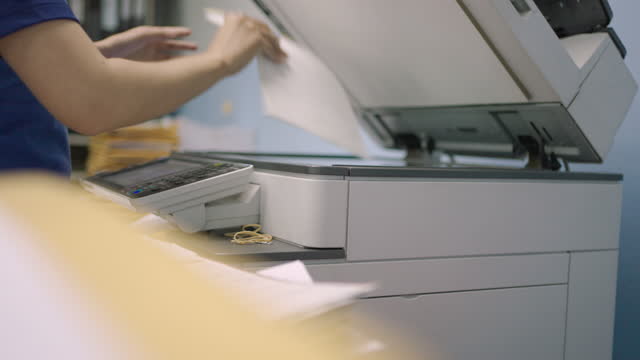 Worker female working on documents by copying documents with a multifunction copier machine.