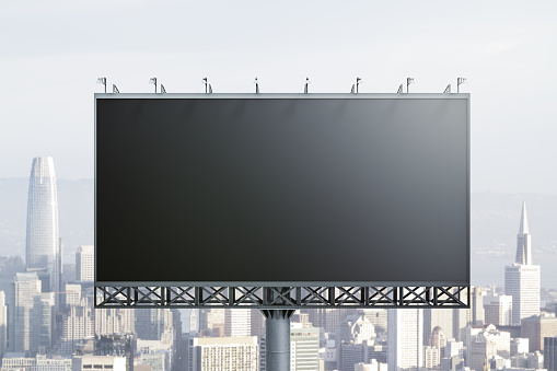 Blank black billboard on city buildings background, front view. Mockup, advertising concept