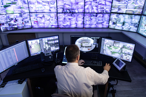 Mature adult man working in surveillance, security and guarding agency and looking at many monitors in front of him.