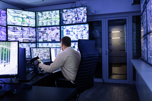 Mature adult man working in surveillance, security and guarding agency and looking at many monitors in front of him.