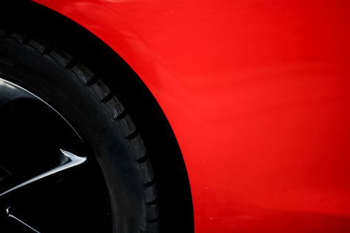 Partial view of a black car tire on a black rim on a red car