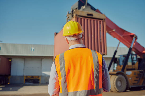istock Forklift truck, logistics or man at a container supply chain, crane delivery service or distribution warehouse. Planning, back view or industry worker with cargo, stock or inventory at shipping port 1473446089