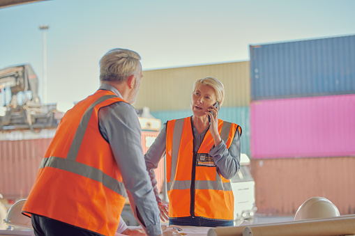 Architect, phone call and logistics in discussion for planning, construction or strategy at depot. Senior woman talking on smartphone in team conversation or industrial project plan at container yard