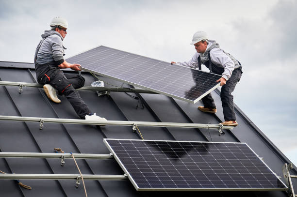 istock Technicians carrying photovoltaic solar module while installing solar panel system on roof of house 1473449851