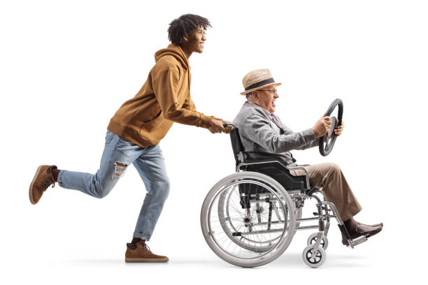 full length profile shot of a young african american man pushing a mature man in a wheelchair holding a steering wheel - physical injury men orthopedic equipment isolated on white imagens e fotografias de stock