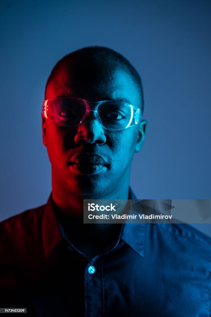 Headshort of an African-American man wearing glasses Headshort of an African-American man wearing glasses and a dark shirt while looking towards the camera, lights are reflected in the glasses against a dark background Portrait Stock Photo