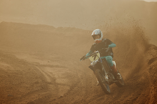 Rear view of dirt bike race riding fast on off-road dirt track.