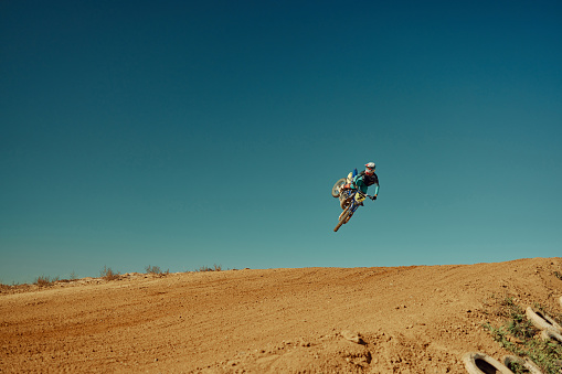 Low angle view of Enduro motocross rider jumping high up off-road at sunset. Copy space.