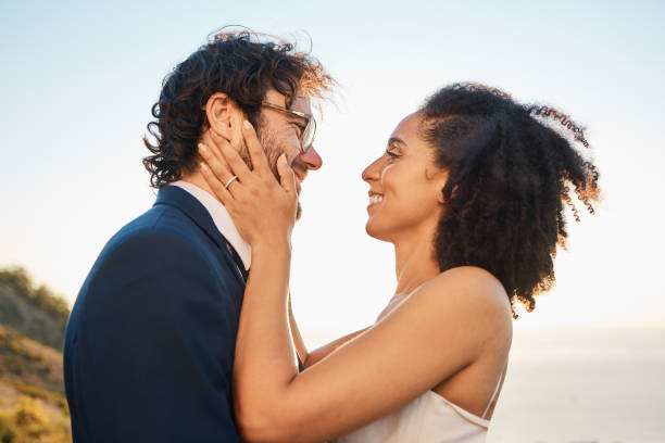istock Wedding, love and interracial couple on mountain for marriage ceremony, commitment and celebration by sea. Romantic holiday, happy and bride and groom bonding, hug and smile by ocean with sunset 1473452135