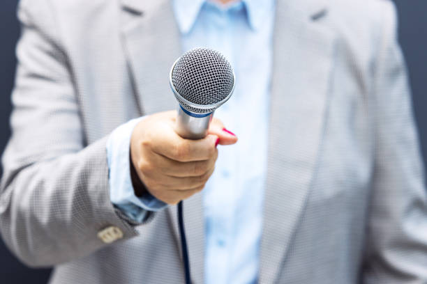 Female journalist holding microphone making media interview stock photo